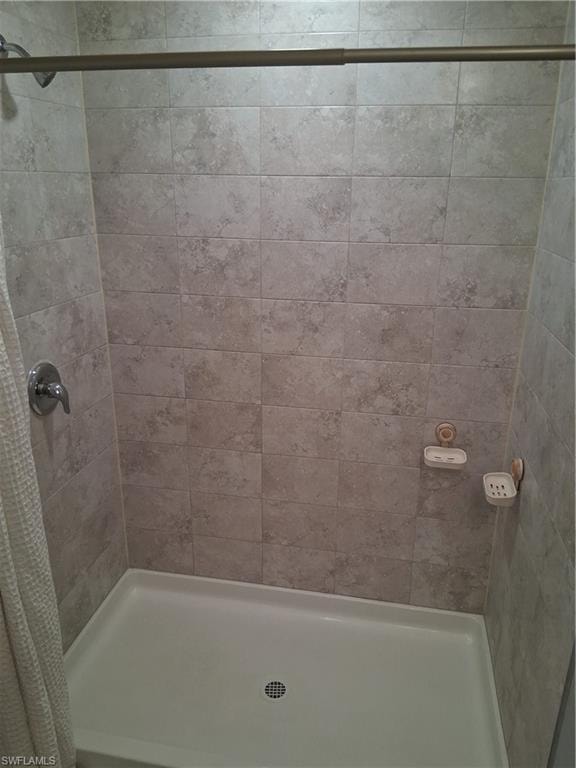 Shower stall featuring light-toned tile walls, a white shower pan, and a chrome shower fixture