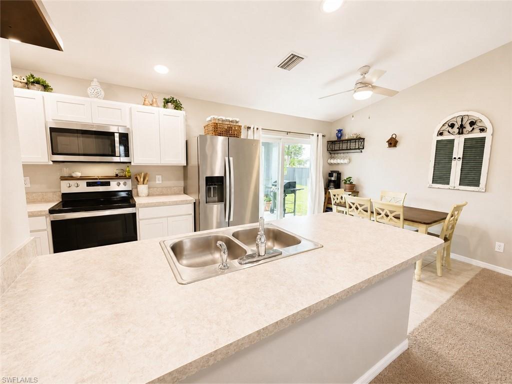 Kitchen with stainless steel appliances, white cabinetry, a double basin sink, and counter seating