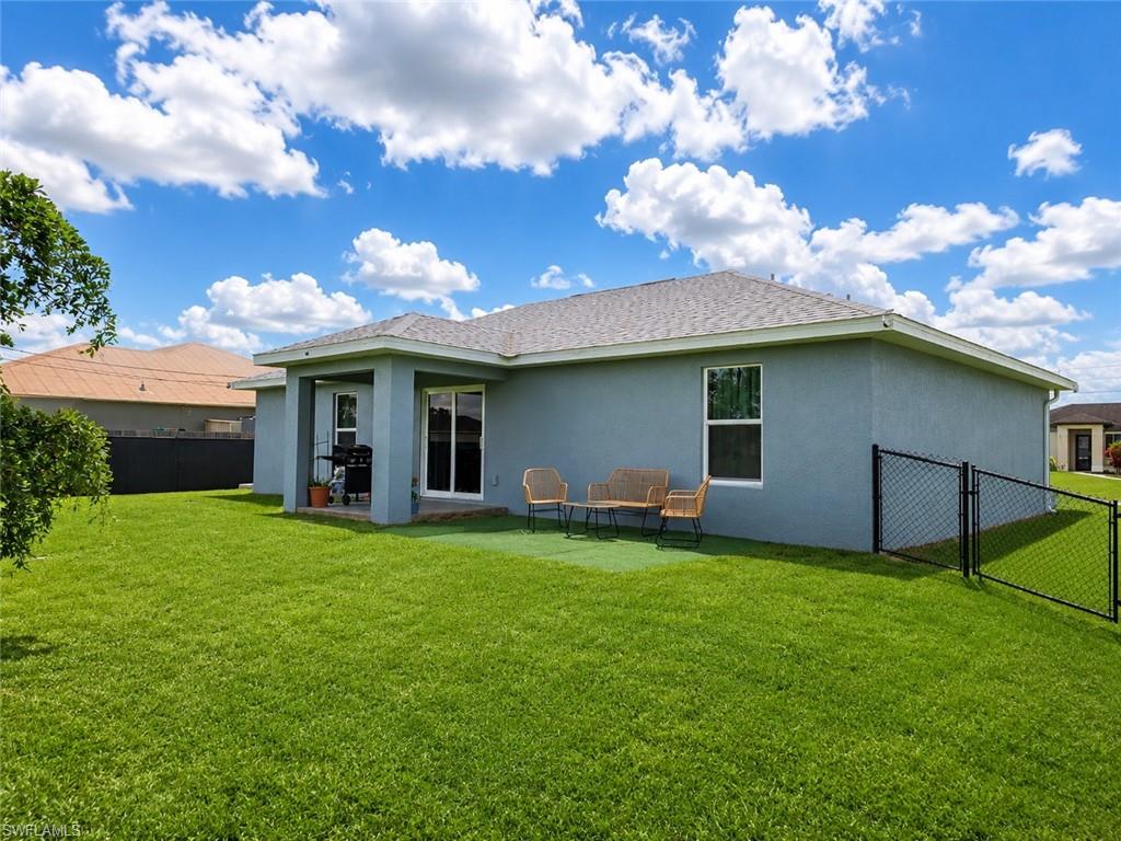 Expansive backyard featuring a manicured lawn, covered patio, sliding glass door access, and a chain-link fence