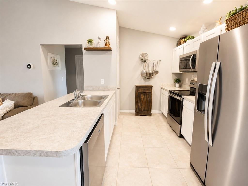 Kitchen featuring stainless steel appliances, white cabinetry, light-toned countertops, tile flooring, and a double basin sink
