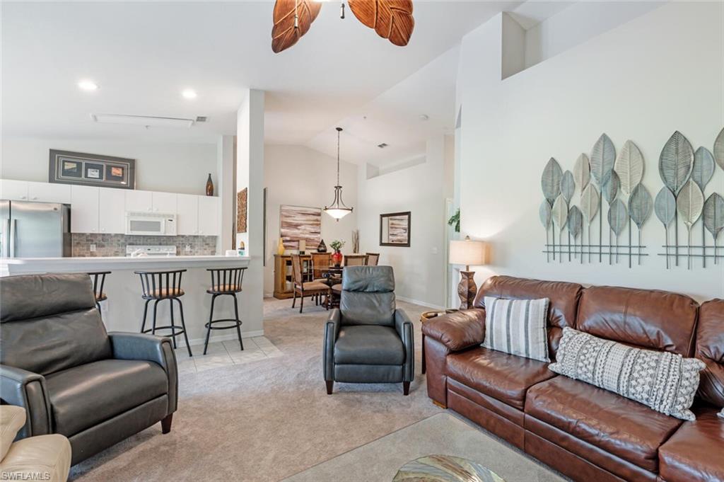 Living room with light colored carpet, high vaulted ceiling, ceiling fan, and light tile patterned floors