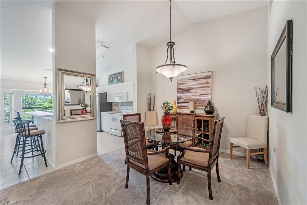 Dining room featuring light tile patterned floors, high vaulted ceiling, light colored carpet, and a chandelier