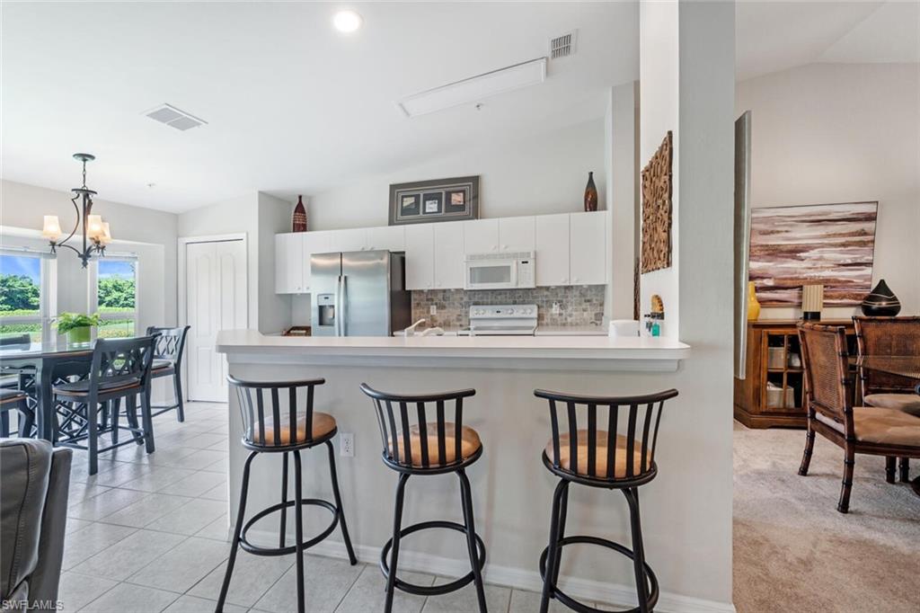 Kitchen with decorative backsplash, a breakfast bar, white appliances, light countertops, and white cabinetry