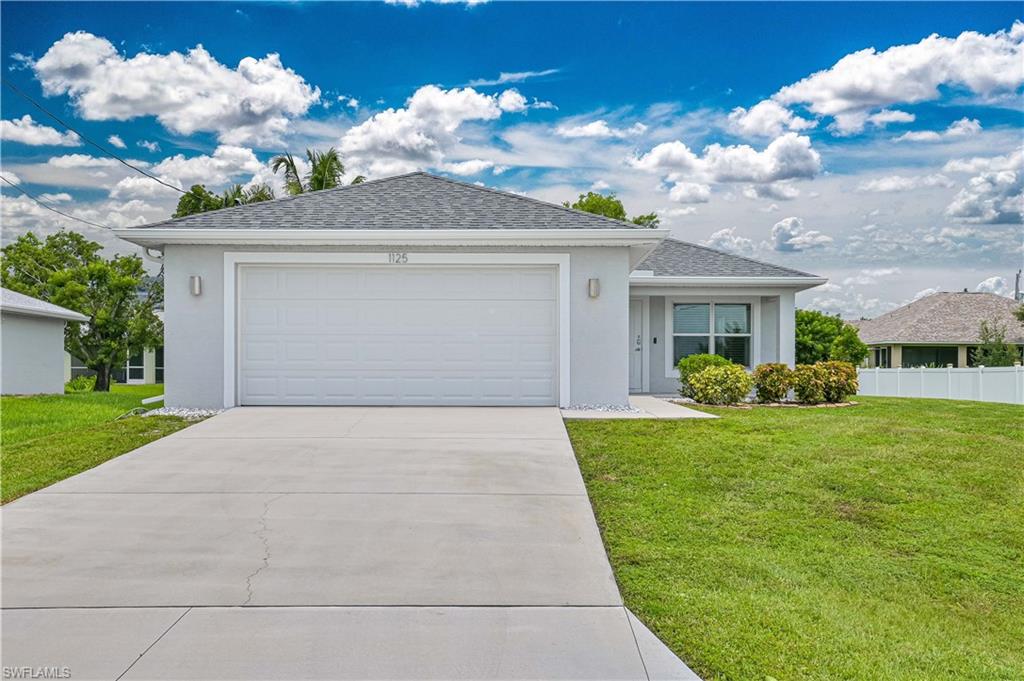 Beautiful front elevation showcasing a modern hip-roof design, oversized two-car garage, extended driveway, manicured landscaping, and a welcoming covered entry. Excellent curb appeal in a growing Northeast Cape Coral location.
