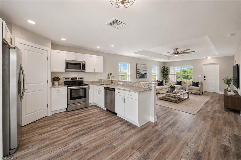 Spacious open-concept kitchen featuring quartz countertops, white shaker cabinets, stainless steel appliances, and a large peninsula overlooking the bright and inviting great room. [Virtually Staged]