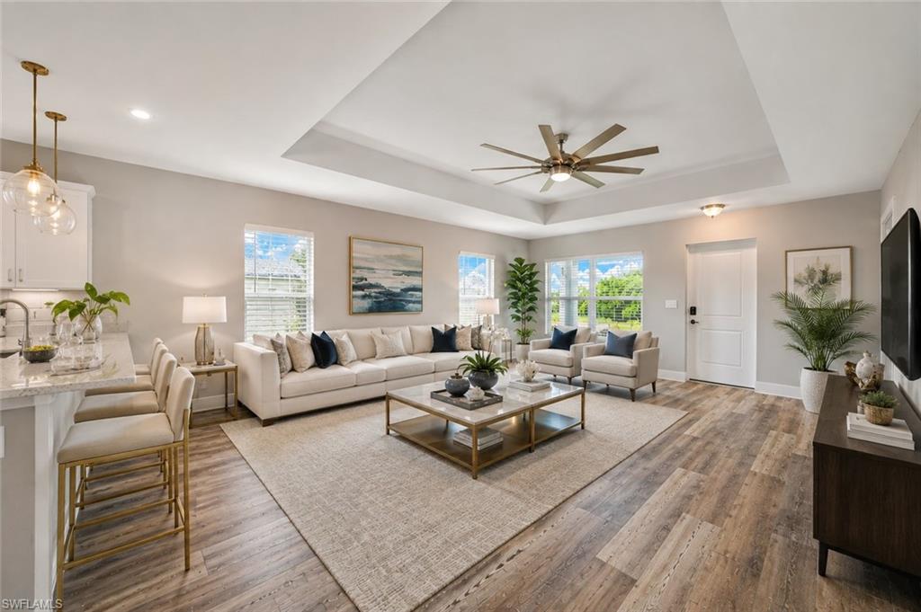 Spacious open-concept living room featuring tray ceilings, luxury vinyl plank flooring, abundant natural light, and seamless flow to the designer kitchen—ideal for everyday living and entertaining. [Virtually Staged]