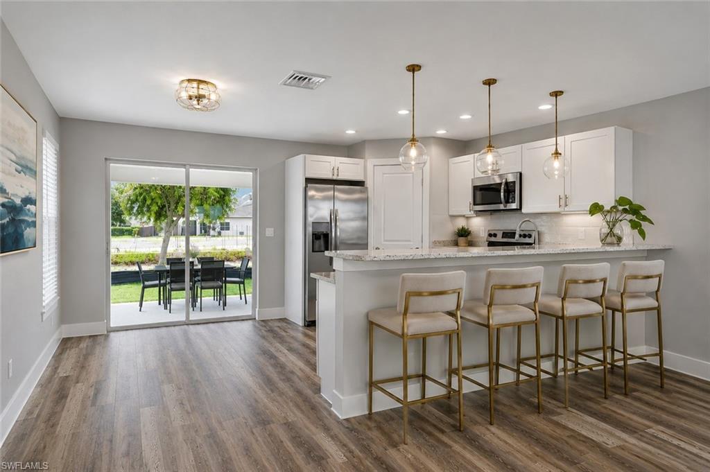 Designer kitchen featuring quartz countertops, white shaker cabinetry, stainless steel appliances, pendant lighting, and a spacious breakfast bar with seating for four. [Virtually Staged]