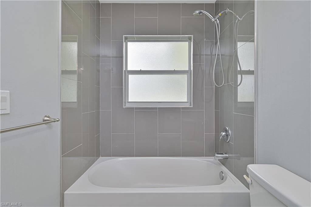 Floor-to-ceiling tiled tub/shower with modern fixtures and a frosted window for abundant natural light and privacy.
