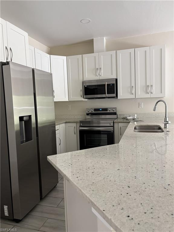 Modern kitchen featuring white shaker cabinetry, stainless steel appliances, speckled countertops, and tile flooring