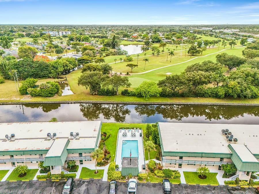 Community buildings featuring a central swimming pool with surrounding lounge chairs, manicured green spaces, and a nearby canal