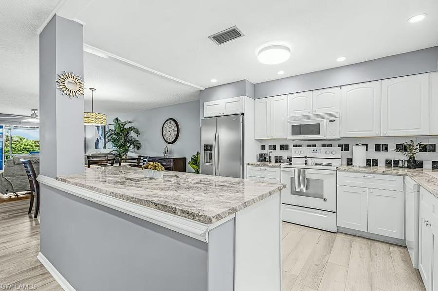 White cabinetry with chrome hardware, full appliance suite, granite-look countertops, black and white tiled backsplash, and wood-finish flooring