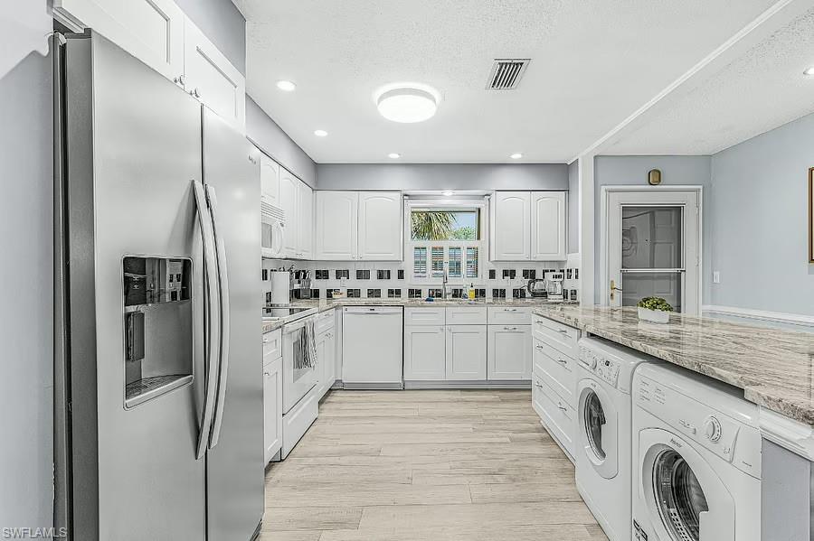 White cabinetry with black square tile backsplash, stainless steel refrigerator, light wood-finish flooring, recessed lighting, and a built-in washer and dryer