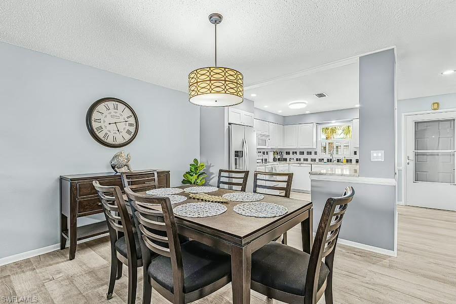 Dining area with wood-finish flooring, a contemporary ceiling light fixture, and a partial wall opening to the kitchen