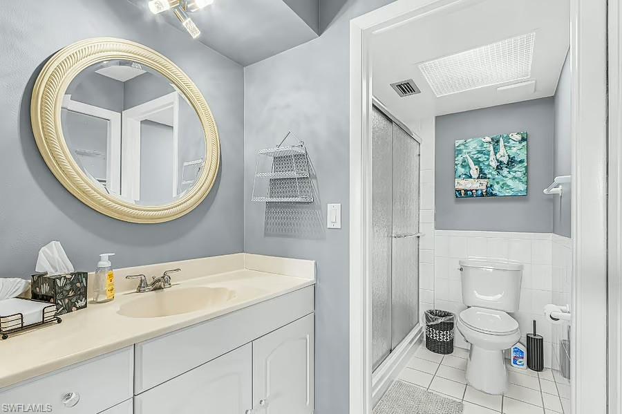 Bathroom featuring a vanity with an integrated sink, a large round mirror, a shower with sliding glass doors, a toilet, and tile flooring