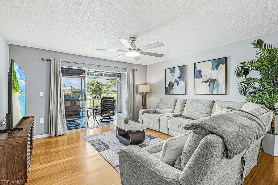 Wood-finish flooring, ceiling fan, and sliding glass door leading to a screened lanai with a water feature backdrop