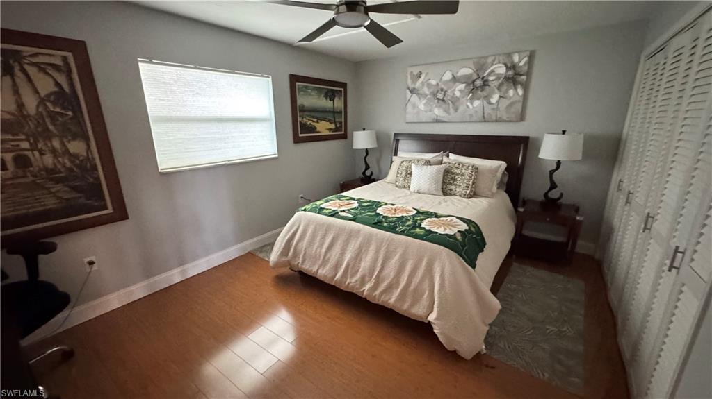 Wood-finish flooring, a ceiling fan with integrated lighting, window with blinds, and white louvered closet doors