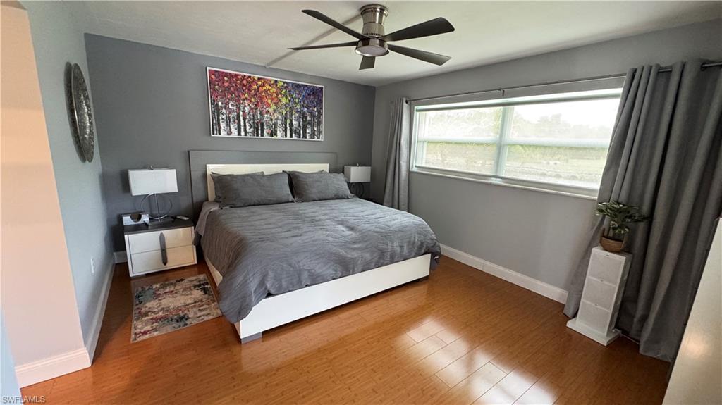 Wood-finish flooring, ceiling fan, and a wide window with curtain rod and drapes