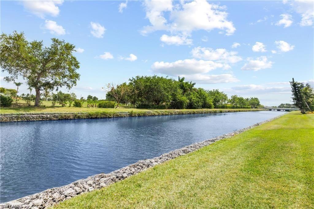Waterfront property featuring a canal, manicured lawn, and mature trees