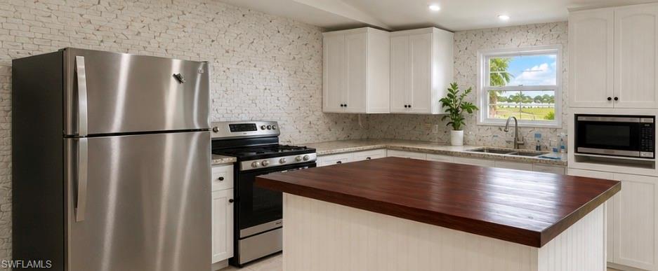 Updated kitchen with stainless steel appliances, white cabinetry, a wood-finish island countertop, and stone-finish backsplash