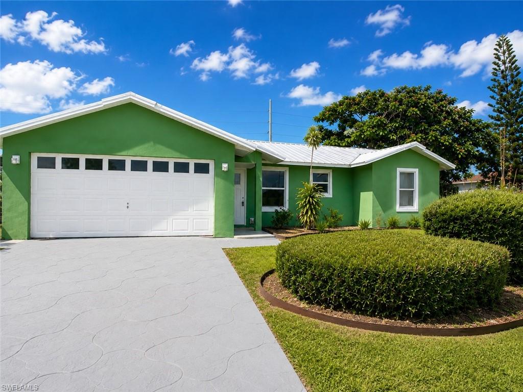 Exterior featuring a white garage door with upper window inserts, a patterned concrete driveway, a metal roof, and manicured landscaping with a circular shrub