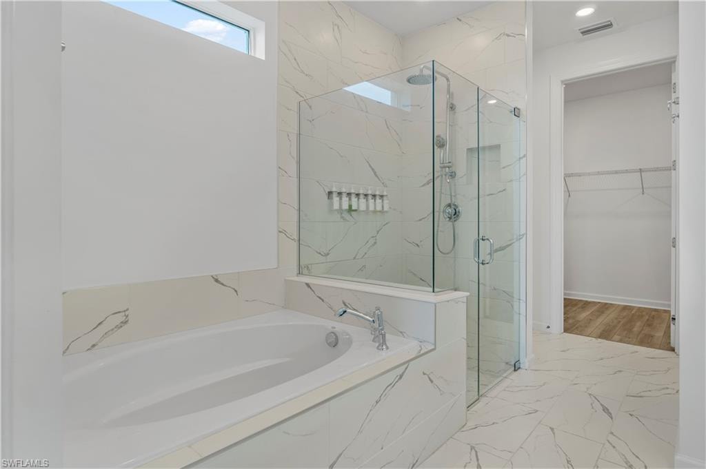 Soaking tub with deck-mounted chrome fixtures, glass-enclosed shower with a rainfall showerhead, and a tiled shower niche