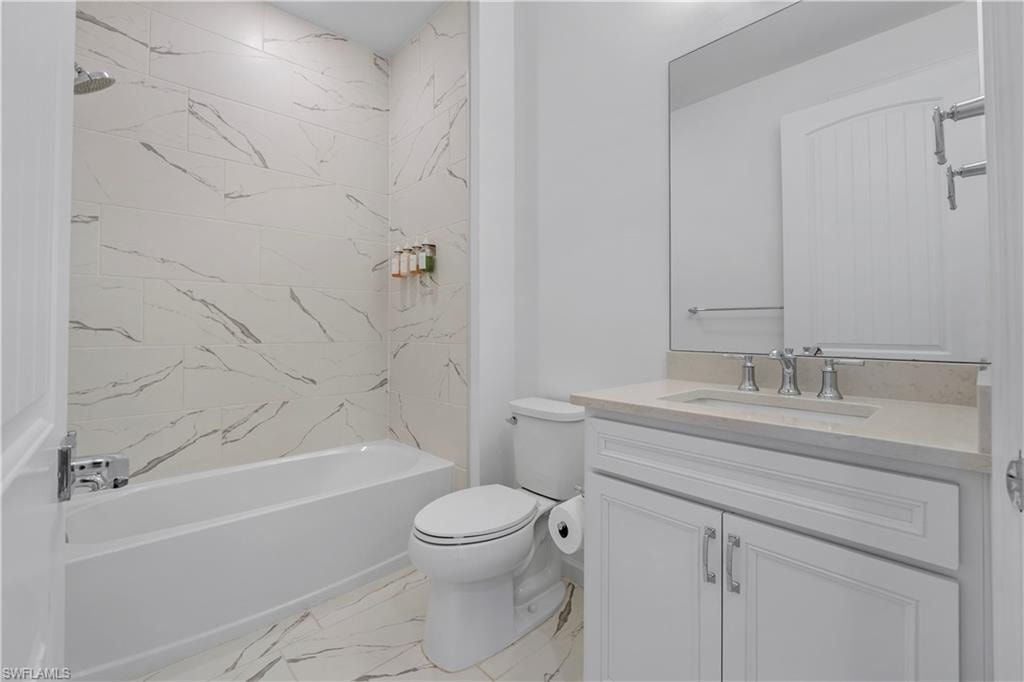 White bathtub with chrome fixtures, large format white and gray veined tile surround, vanity with white shaker-style cabinetry, undermount sink, and light-toned countertop