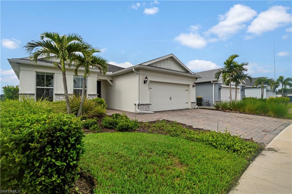 Stucco exterior with stone accenting, paver driveway, attached two-car garage, and mature landscaping