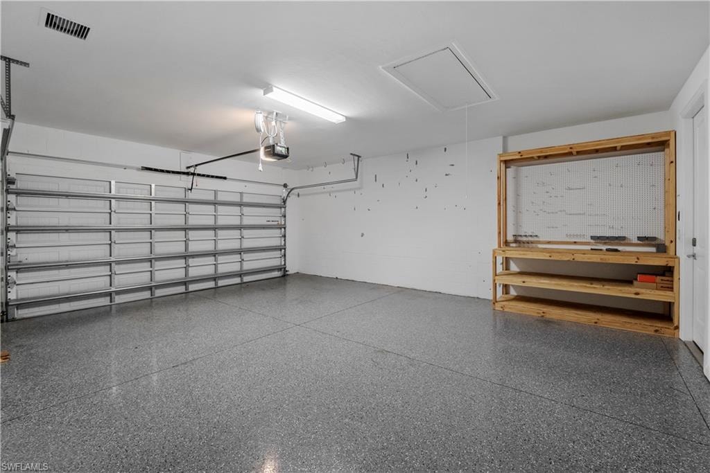 Attached garage featuring a patterned epoxy floor, automatic garage door opener, overhead lighting, and built-in shelving