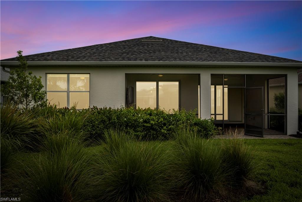 Exterior stucco finish, screened patio, asphalt shingle roof, mature landscaping, and rectangular windows