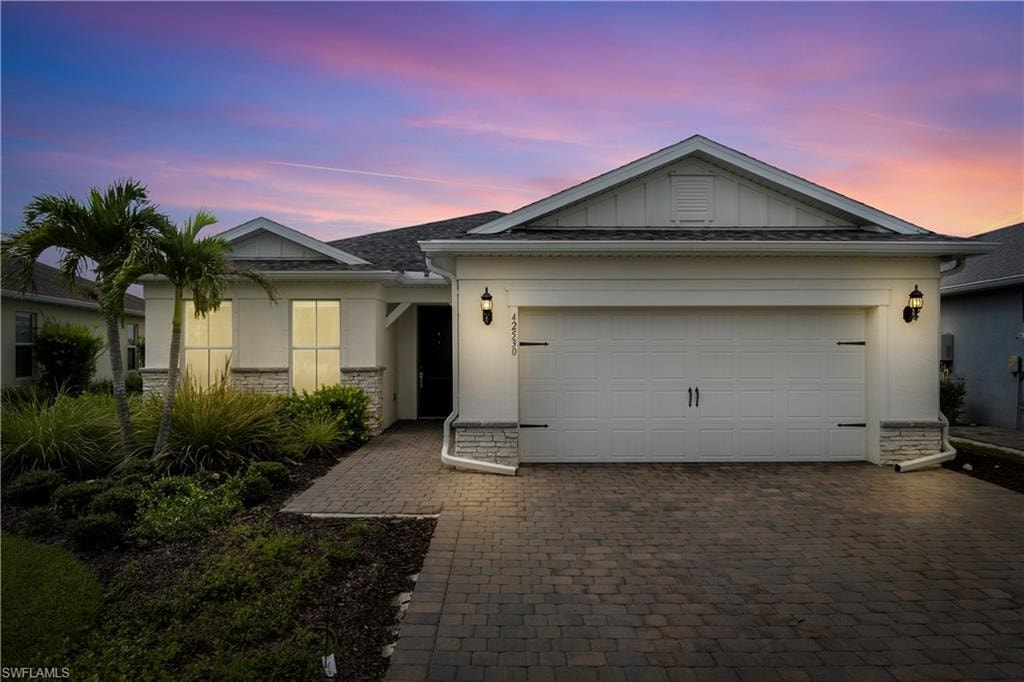 Contemporary exterior with white siding, stone veneer accents, an attached garage, and a paver driveway