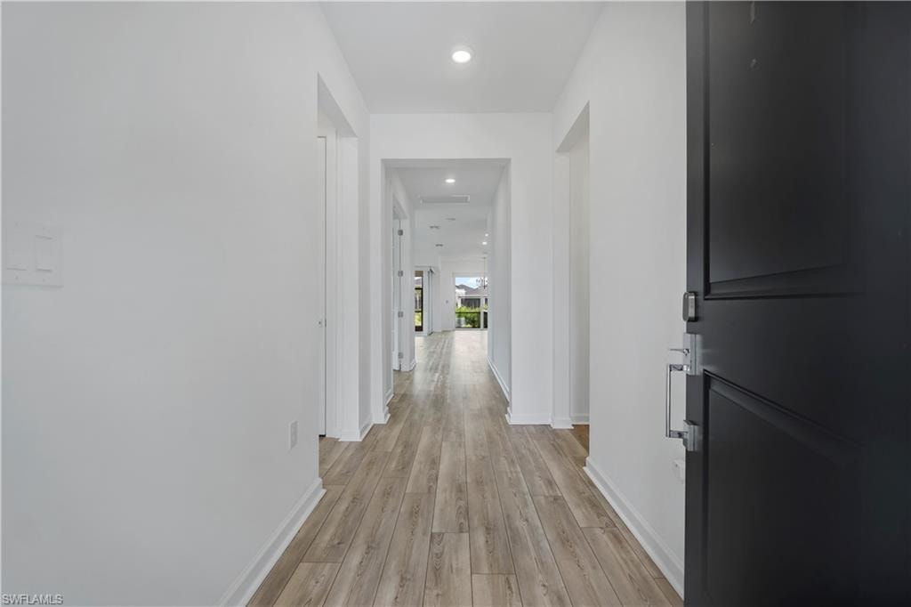Entryway featuring a dark paneled door with contemporary hardware, wood-finish flooring, recessed lighting, and crisp white walls