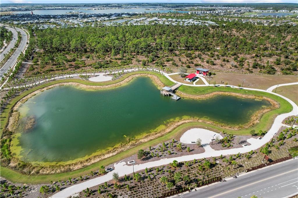 Expansive water feature with a wooden dock, surrounded by paved walking paths, a red-roofed pavilion, and varied landscaping