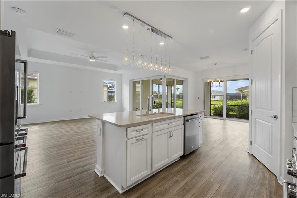 Open-concept living space featuring wood-finish flooring, a kitchen island with integrated sink, and white cabinetry