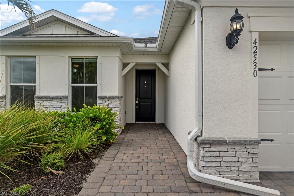 Paver walkway leading to an entryway with a black door, exterior wall light, and a two-car garage