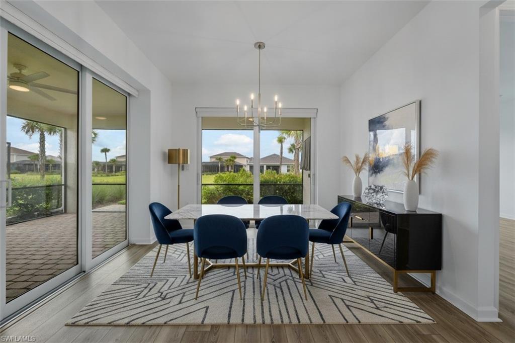 Spacious dining area featuring wood-finish flooring, a contemporary chandelier, a large window, and sliding glass doors opening to an outdoor patio with brick pavers