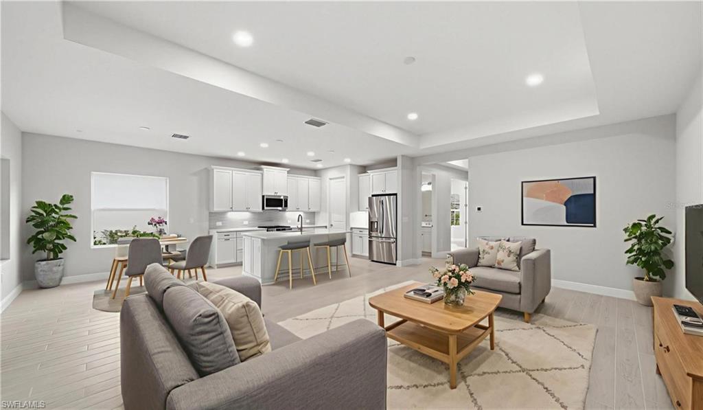 The heart of the home unfolds in this spacious great room, where soaring tray ceilings, abundant recessed lighting, and neutral coastal finishes create a bright, airy atmosphere. The open-concept layout flows seamlessly into the kitchen and dining areas, allowing family and guests to gather comfortably while enjoying views that extend throughout the home's expansive living spaces.