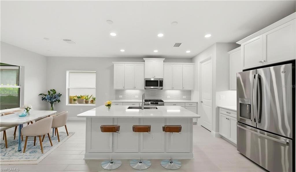 The oversized island serves as the centerpiece of this chef-inspired kitchen, offering generous seating, abundant prep space, and effortless interaction with the surrounding living areas. Crisp white cabinetry, quartz countertops, stainless steel appliances, and a spacious walk-in pantry combine functionality and style, while the open breakfast area creates the perfect spot to enjoy morning coffee before a day on the golf course.