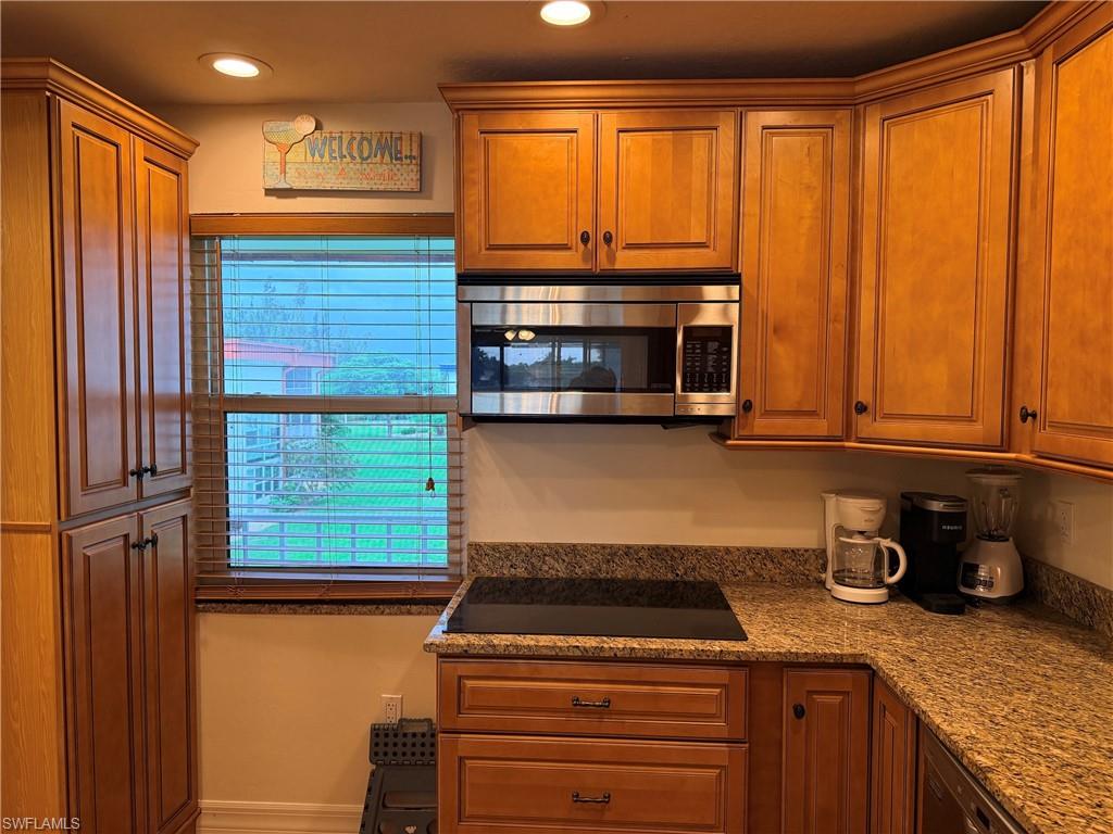 Wood cabinetry with crown molding, stainless steel microwave, cooktop, granite countertops, and recessed lighting