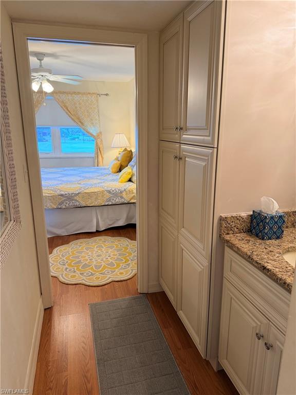 Wood-finish flooring, built-in storage cabinetry, vanity with granite-style countertop, and a ceiling fan with integrated lighting
