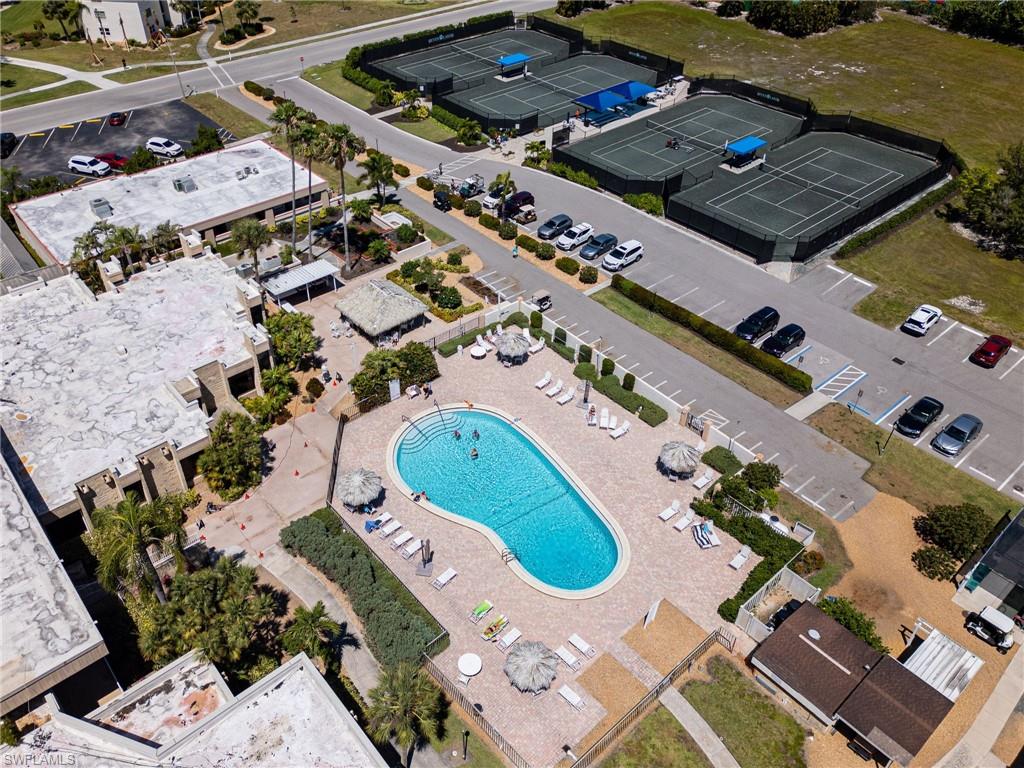 Outdoor swimming pool with surrounding paver decking, multiple tennis courts, and ample parking facilities