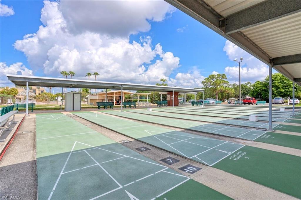 Multiple shuffleboard courts with covered seating areas, surrounded by mature landscaping