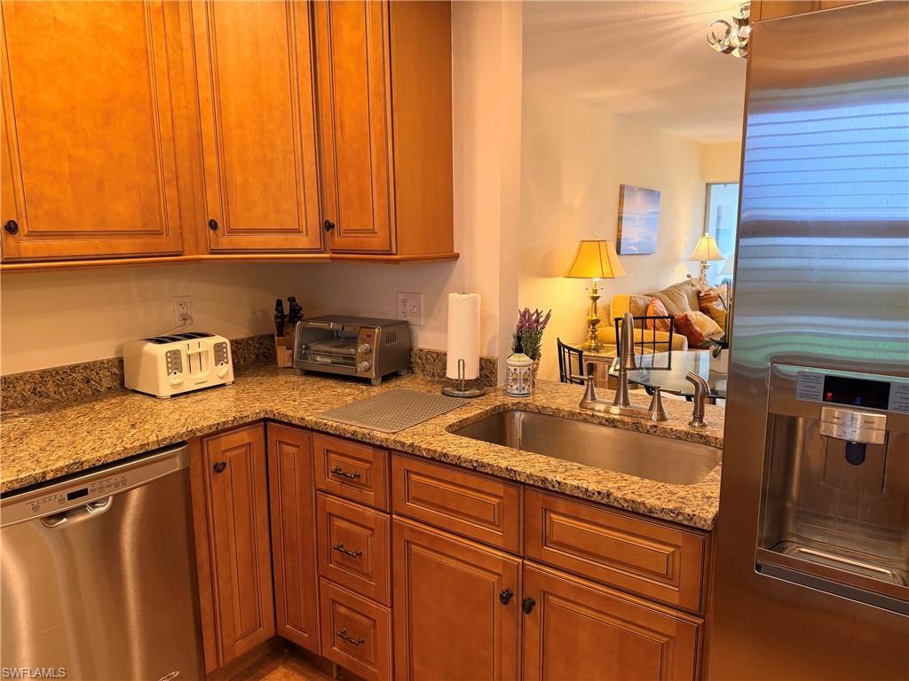 Wood cabinetry with dark hardware, granite countertops, stainless steel sink with a gooseneck faucet, and stainless steel dishwasher