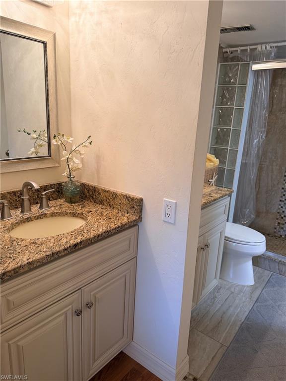 Vanity with granite countertop and undermount sink, wood-finish flooring, and a shower with glass block wall and tiled floor