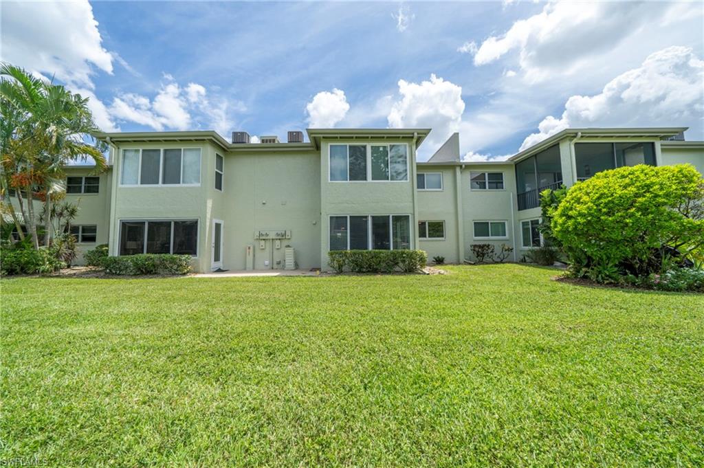 Expansive green lawn with a building featuring a stucco exterior, multiple windows, and a screened-in porch