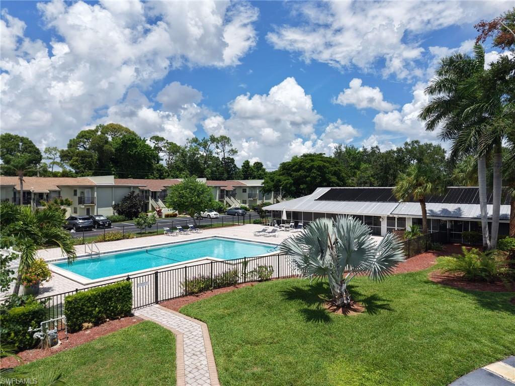 Community swimming pool with a black wrought iron fence, surrounded by green lawn and tropical landscaping