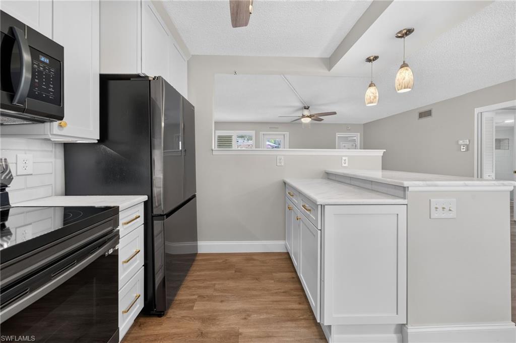Full-size black refrigerator, black microwave, white cabinetry with gold-tone hardware, wood-finish flooring, and pendant lighting