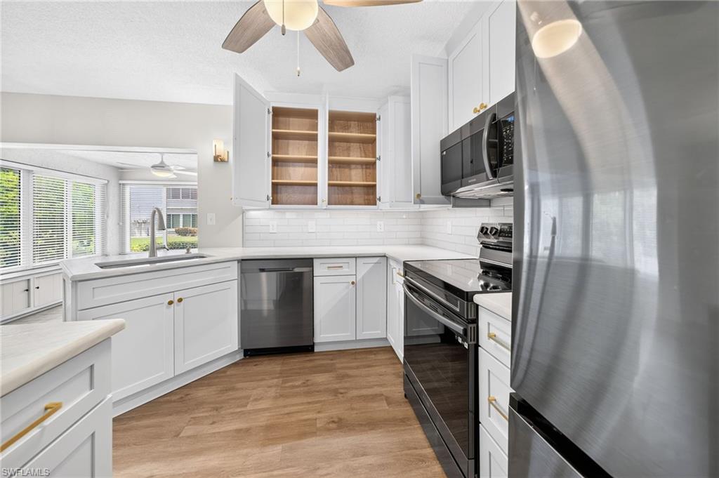 White shaker cabinetry with gold-tone hardware, stainless steel appliances, wood-finish flooring, and white subway tile backsplash