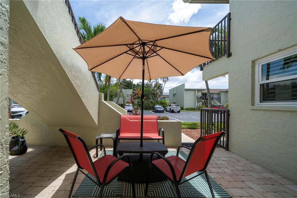 Covered patio with tan umbrella and red sling chairs, black round table, brick flooring, and stucco walls