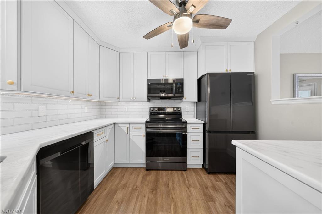 Kitchen featuring white cabinetry, light-toned countertops, black appliances, subway tile backsplash, and wood-finish flooring