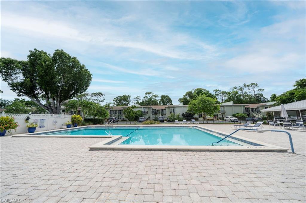 Resort style paver patio with a large swimming pool, surrounded by lush landscaping and mature trees